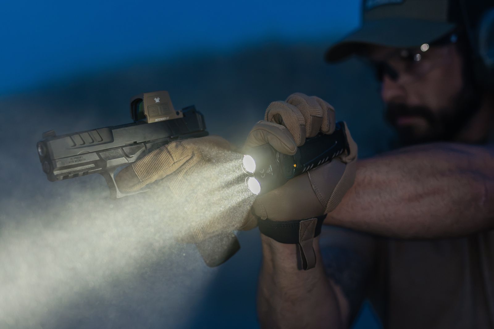 Man aiming a handgun while holding a tactical flashlight, illuminating the area with a powerful beam of white light.